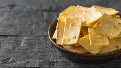 Mexican tortilla chips with cheese in a clay bowl on a black wooden table.