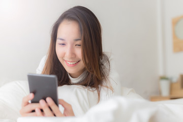 Happy women playing smartphone and smile on bed after wake up in the morning