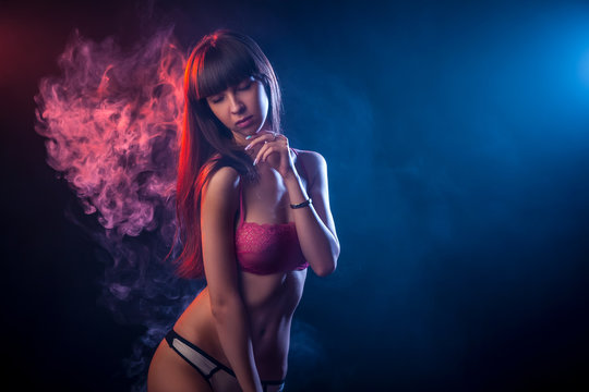 Young dark-haired woman in red lingerie posing against a background of red and red smoke from a wipe on a black isolated background
