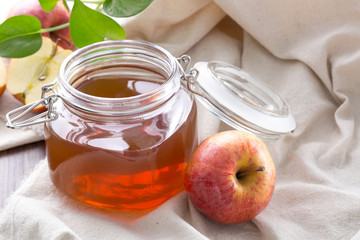 Closeup of glass jar apple juice with fresh apples on table