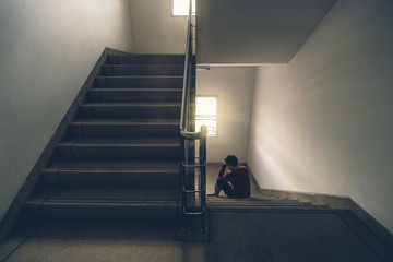 Depressed man sitting head in hands on the staircase in the fire escape or building stair with low...
