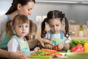 Happy mother and her daughters enjoy making healthy meal together at their home