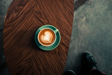 Turquoise mug of flat white coffee with heart shaped latte art on wooden table at the hipster coffee shop.  Vintage color filter effect. Flat lay, copyspace 