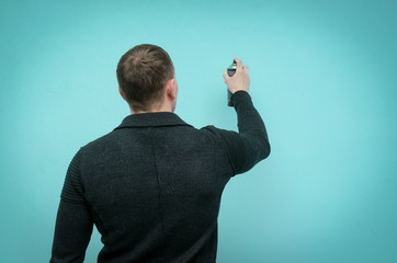 Rear view of a man drawing a graffiti on a wall with a ballon with paint isolated on blue background.