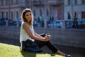 Female sitting on the grass drinking coffee in a cardboard Cup