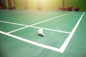 White badminton shuttlecock on a green floor with blurred players in badminton court