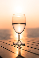 Silhouette glass of wine on a wooden table with  seascape and skyline in the evening with sunset tone style.