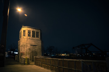 Vintage industrial city bridge with tower house and urban sidewalk at night.