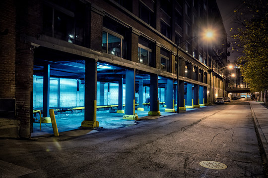 Dark City Downtown Street Road And Alley At Night With An Industrial Warehouse Loading Dock.