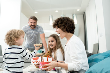 Portrait of happy young family with two children celebrating Valentines day  at home with adorable little boy giving presents in foreground