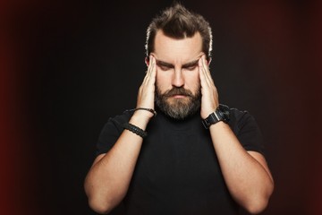 Terrible headache. Frustrated man touching head with hands and making face while standing against black background. It is surrounded by a red glow, symbolizing pain and suffering. Copy space for text