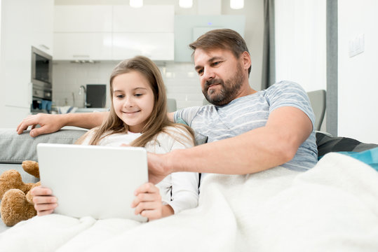 Portrait of bearded father using laptop in bed enjoying evening with teenage daughter and watching movies