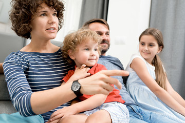 Portrait of happy young family with two children watching TV sitting on sofa in living room and discussing movies