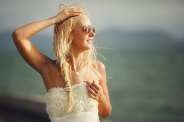Fototapeta na wymiar woman with sunglasses and white wedding dress on sea background.