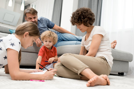 Portrait of happy  family of four spending evening together drawing with children on floor in living room