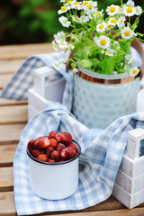 june or july garden scene with fresh picked organic wild strawberry and chamomile flowers on wooden table outdoor. Summertime still life, healthy country living on farm concept