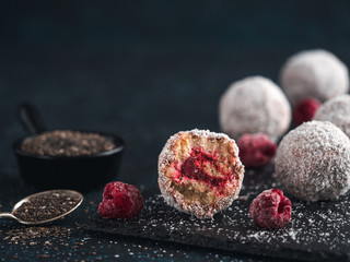 Raw vegan lamington bliss balls with raspberries chia jam on dark background. No baked healthy vegan sweet dessert idea and recipe. Copy space for text.