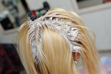 A blond girl was smeared with paint on her hair in a beauty salon