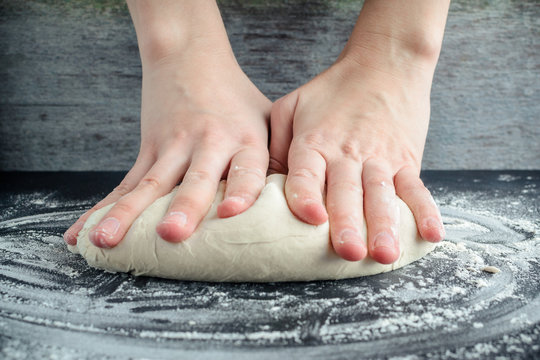 woman kneads dough on a wooden table