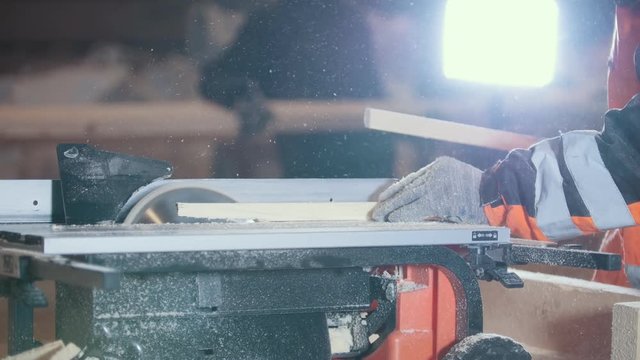 Worker joiner cutting wooden plank with dangerous circular electric saw, profile view