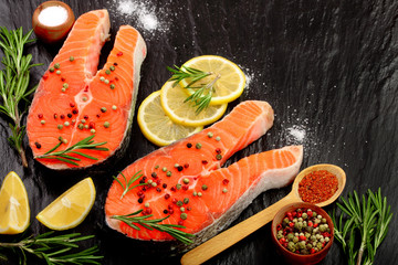 Slice of red fish salmon with lemon, rosemary on black stone background with copy space for your text. Top view