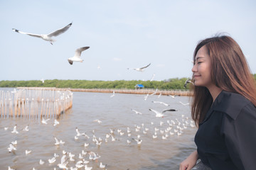 Closeup image of a beautiful asian woman with a flock of seagulls flying above the sea with blue sky background
