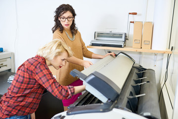 Portrait of two women setting up plotter machine in printing shop, focus on  manager giving instructions to employee, copy space