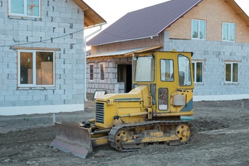 Yellow crawler bulldozer on the background of houses under construction