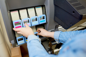 Close up view of female hands taking out color marked ink tanks from plotter in printing shop or...
