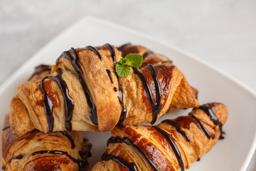 Fresh croissants with chocolate syrup on a light background, copy space. French cuisine dessert concept.