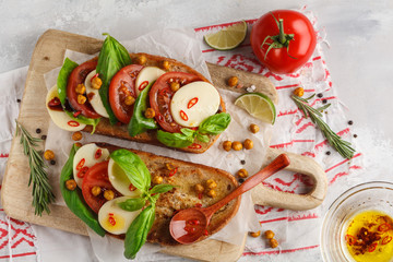Caprese sandwich with mozzarella, tomato, fried chickpeas and basil on a wooden board, top view, copy space. Italian cuisine concept.