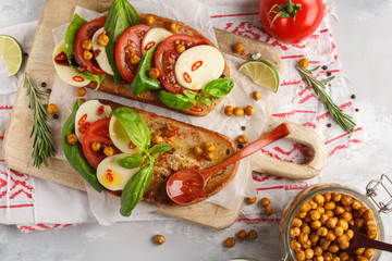 Caprese sandwich with mozzarella, tomato, fried chickpeas and basil on a wooden board, top view, copy space. Italian cuisine concept.