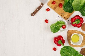 Cooking fresh spring salad of green and red vegetables, spices on white wooden background, border, top view.