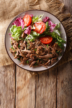 Delicious food: slow cooked pulled beef with fresh vegetable salad close-up. Vertical top view from above
