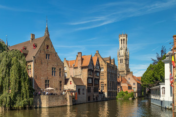 Naklejka premium Kanał Rozenhoedkaai w Brugii z dzwonnicą w tle. Typowy widok na Brugię (Brugge) w Belgii z domami z czerwonej cegły z trójkątnymi dachami i kanałami.