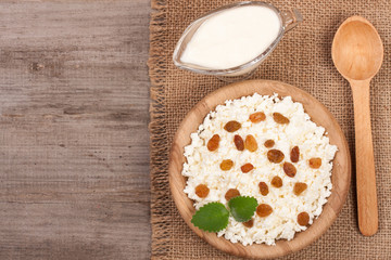 Cottage cheese in bowl with sour cream and raisins on old wooden background with copy space for your text. Top view