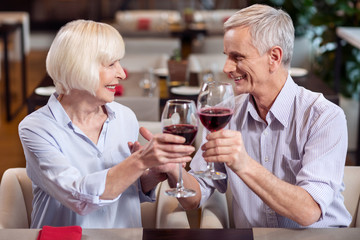 Great wine. Joyful merry mature couple carrying glasses of wine while talking and posing in profile