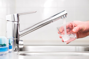 Filling glass with tap water. Modern faucet and sink in home kitchen. Man pouring fresh drink to...