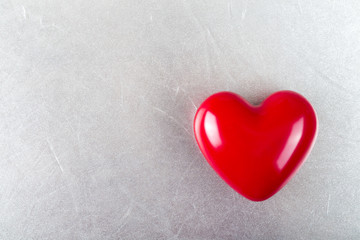 Red glossy heart on silver texture background.