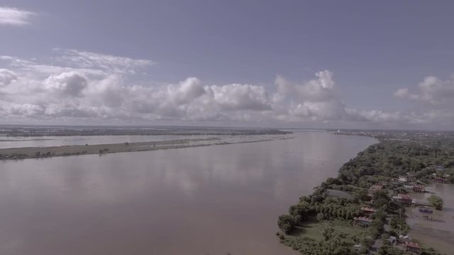 Aerial drone shot: Flying down over floods affected houses with rising water along the river and drowning fields in a rural area. The main road still passable by cars and motorcycles