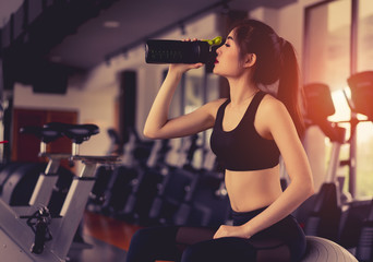 Asian woman drinking protein shake from bottle after workout exercise for muscle at fitness gym...