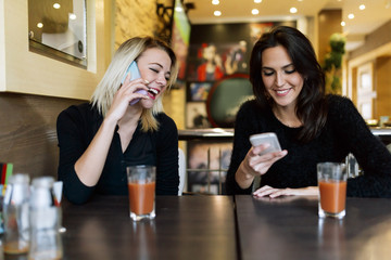 Two beautiful women talking on phone in cafe