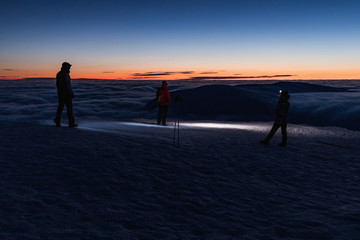 The peak of the Snezka Mountain in winter in the Krkonose Mountains. Group of tourists with lights on the summit of Snezka.