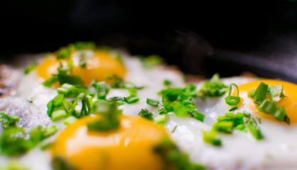 Fried chicken eggs with greens and spring onions in a frying pan.