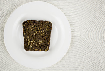 Black bread with seeds on a white plate.