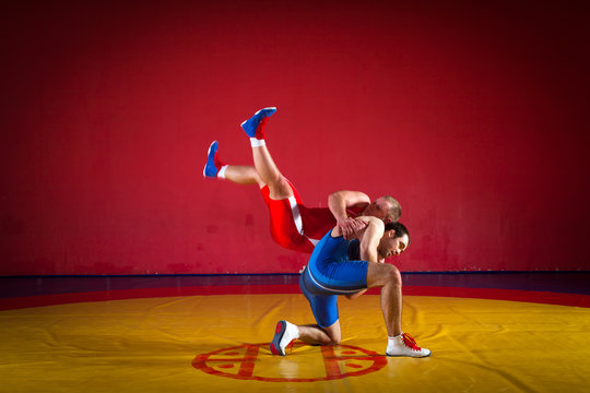 Two greco-roman  wrestlers in red and blue uniform wrestling   on a yellow wrestling carpet in the gym