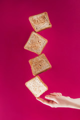 partial view of woman holding levitating toasts on finger isolated on pink
