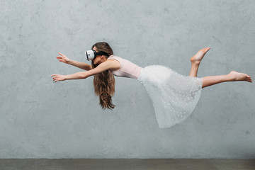 young barefoot woman in virtual reality headset levitating on grey