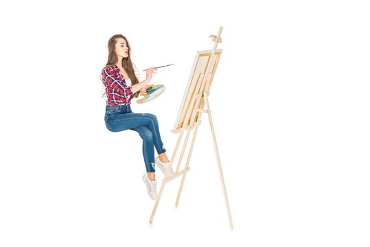 young woman levitating and painting on easel isolated on white