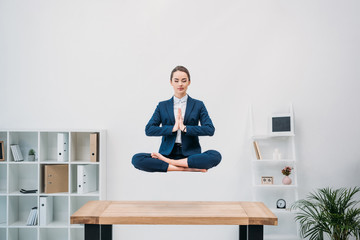 young businesswoman with closed eyes meditating while levitating at workplace